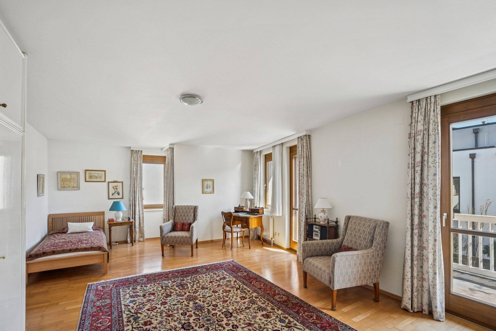Geräumiges Schlafzimmer mit Parkettboden, Teppich und Zugang zu einem Balkon durch Fenstertüren.