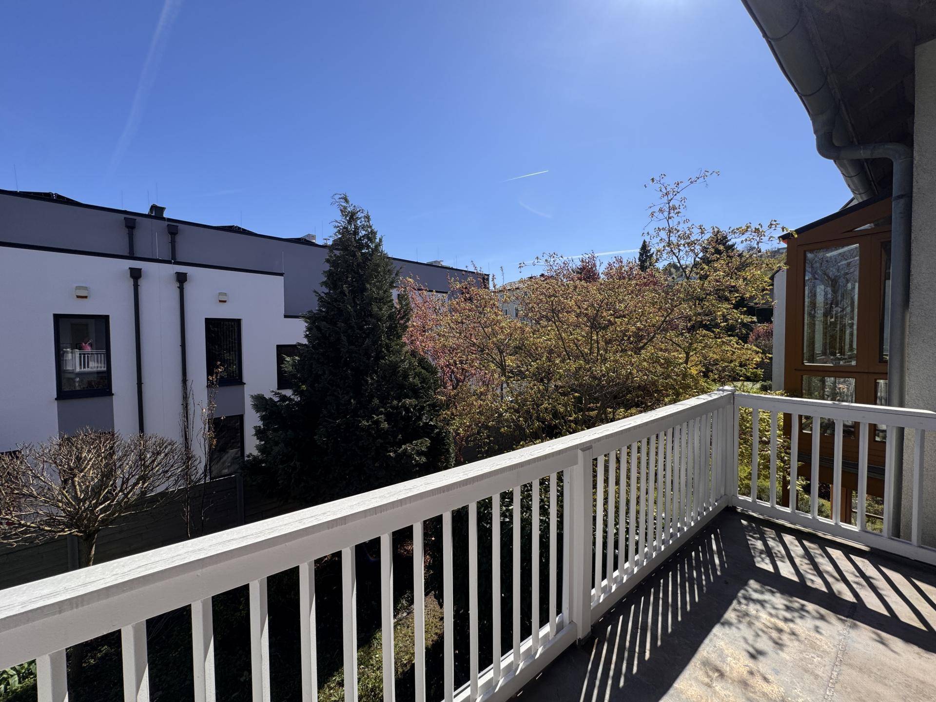 Sonnenverwöhnter Balkon mit weißem Geländer und Blick auf die umliegenden Gebäude und Bäume.