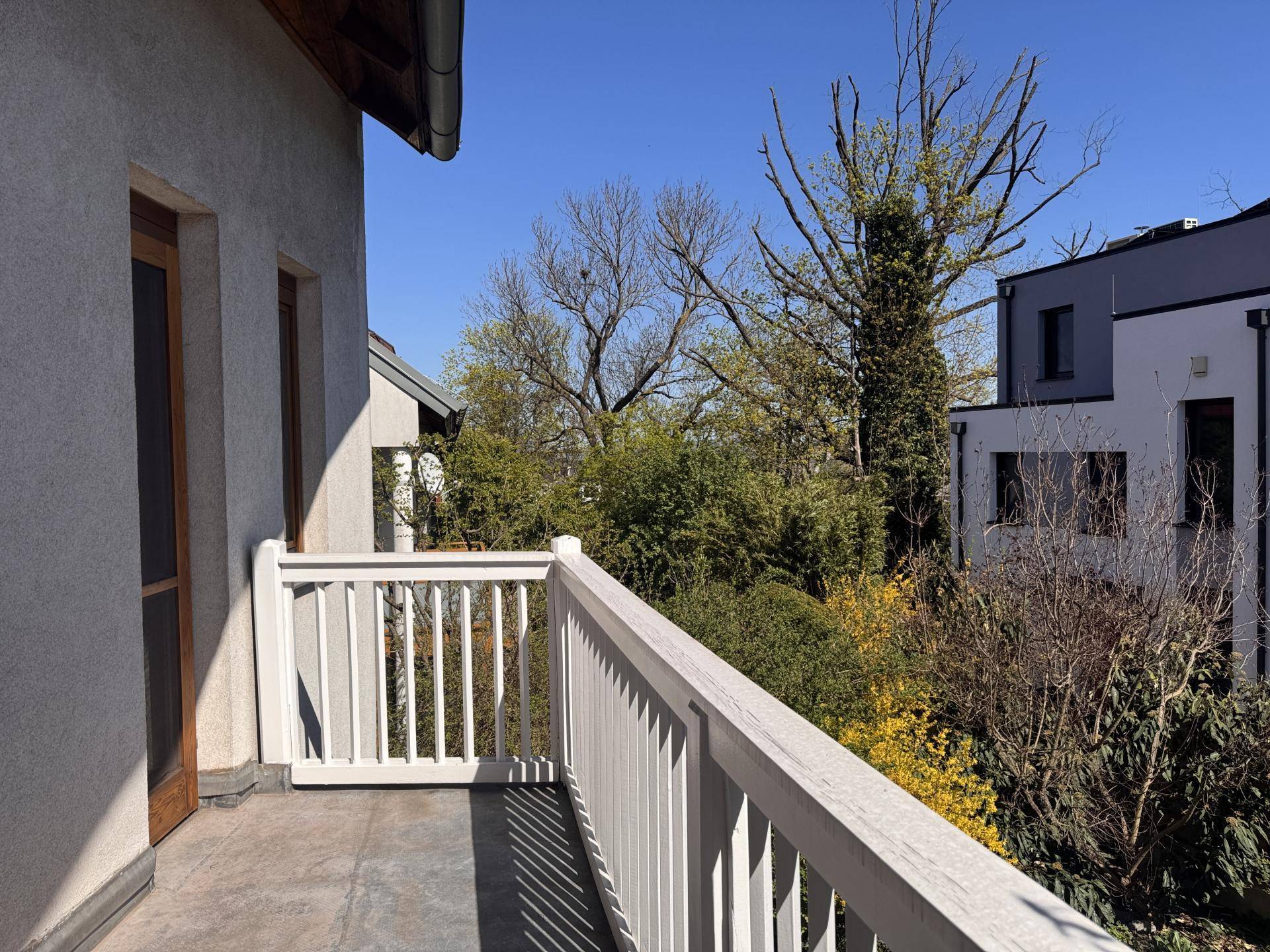 Balkon mit weitem Blick ins Grüne und auf benachbarte Häuser unter blauem Himmel.