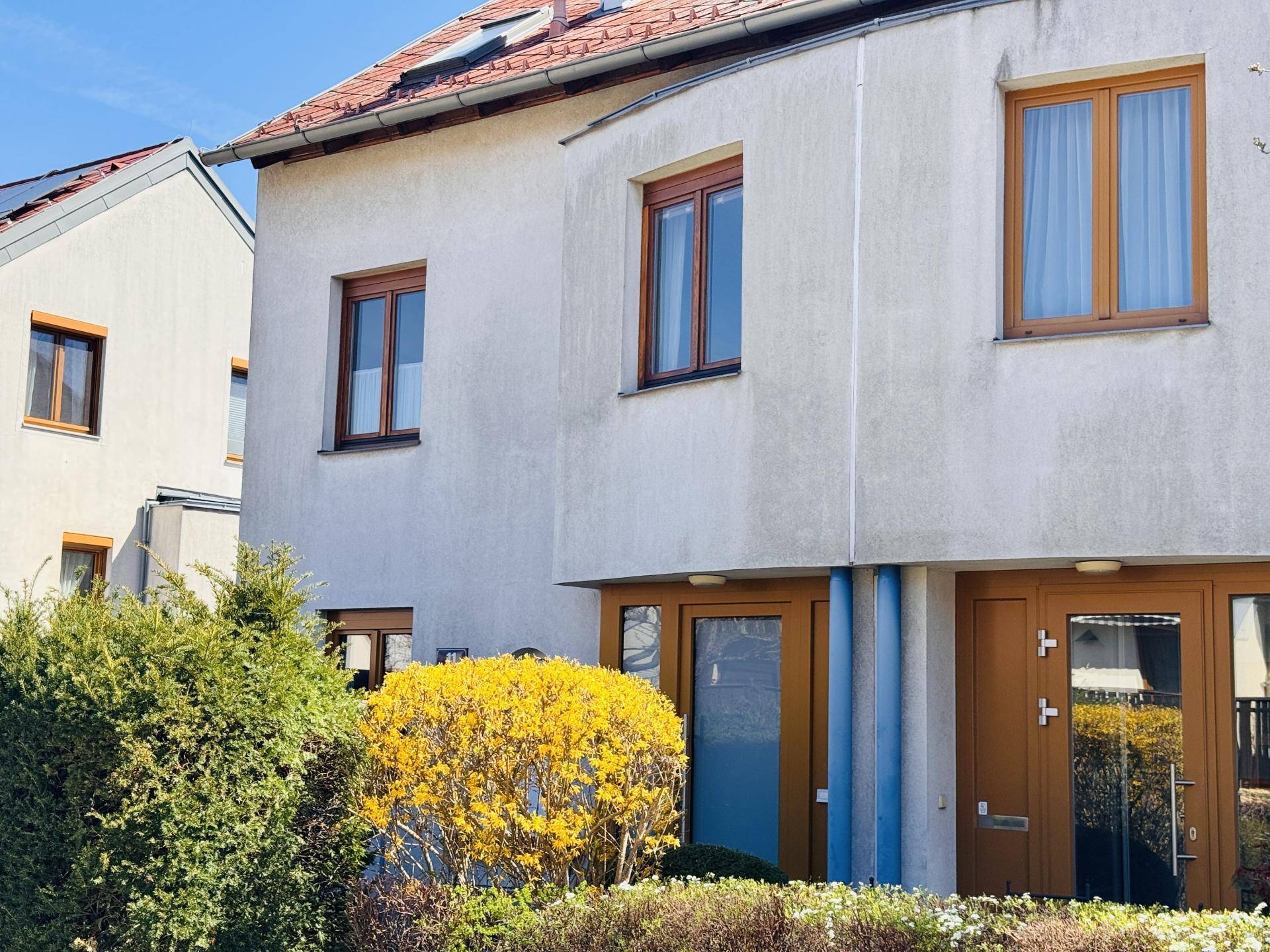 Vorderansicht des Hauses mit mehreren Fenstern und einer modernen Eingangstür in hellem Holzton.