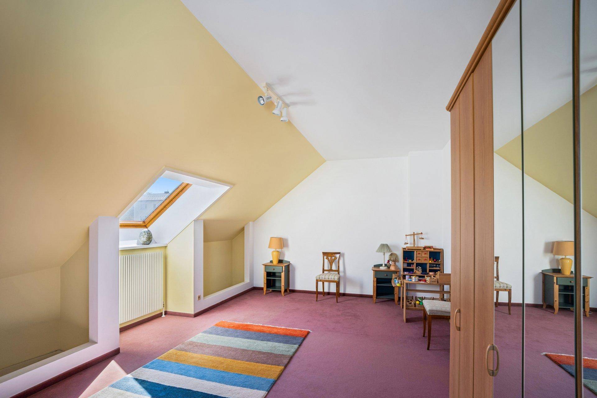 Helles Dachzimmer mit Teppichboden, Dachfenster und schrägen Wänden, ideal als Kinderzimmer oder Büro.