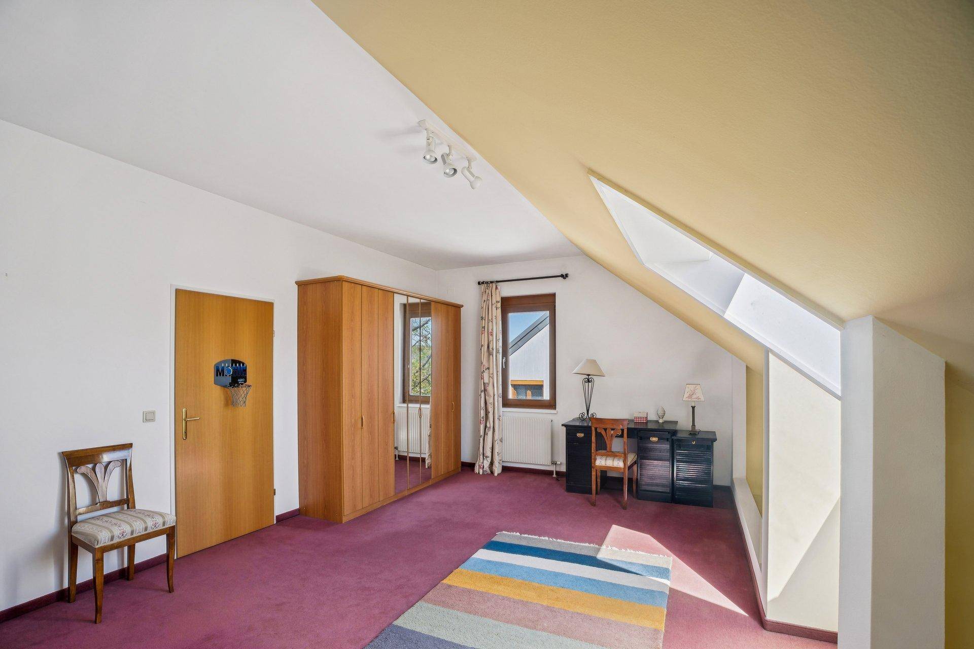 Dachzimmer mit Teppichboden, Dachfenster und Kleiderschrank, genutzt als vielseitiger Wohnraum.