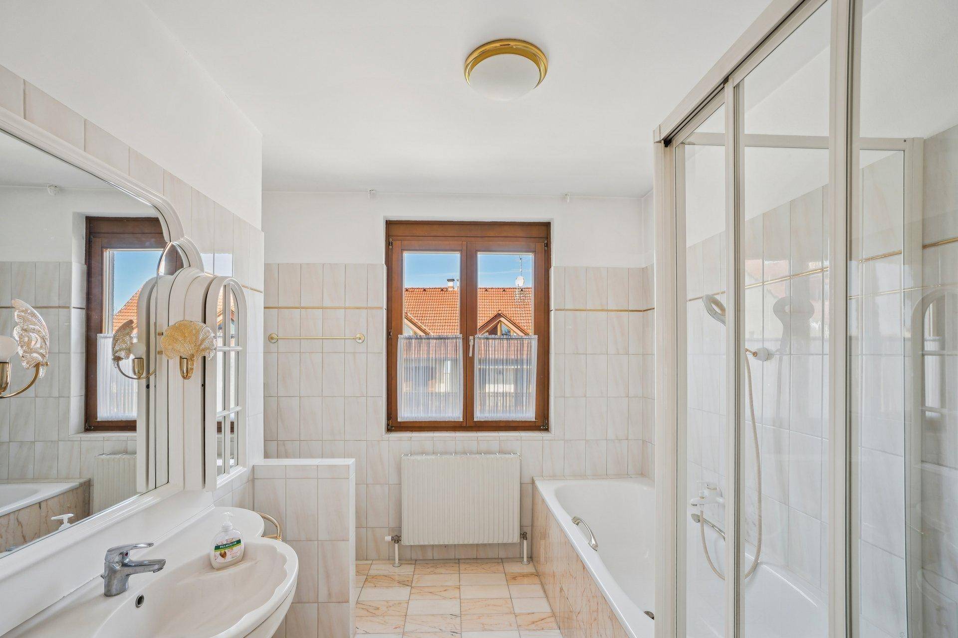 Helles Badezimmer mit Badewanne, Duschkabine, Fenster und hellen Fliesen.