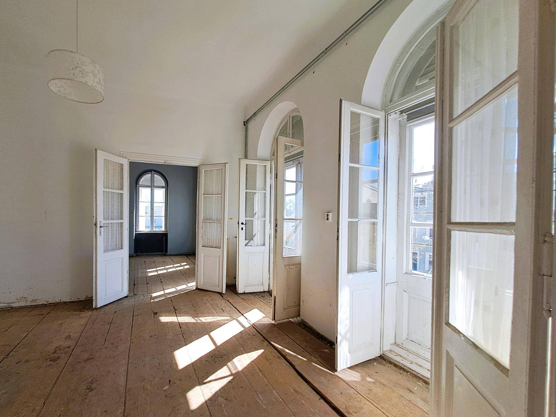 Geräumiger Raum mit Holzdielenboden, hohen Decken und eleganten Rundbogenfenstern.