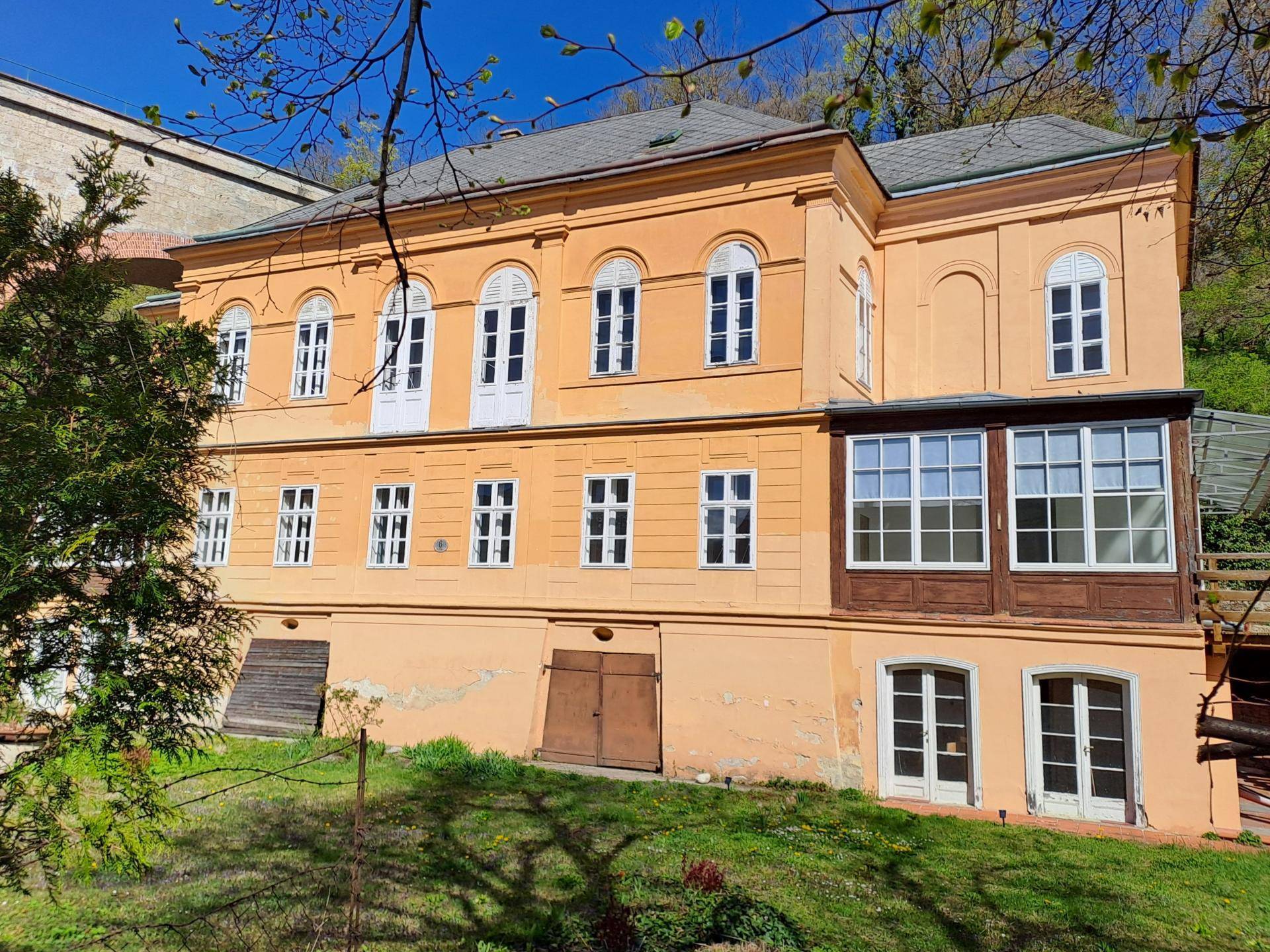 Fassade des historischen Gebäudes mit Wintergarten und großen Fenstern, umgeben von Natur.