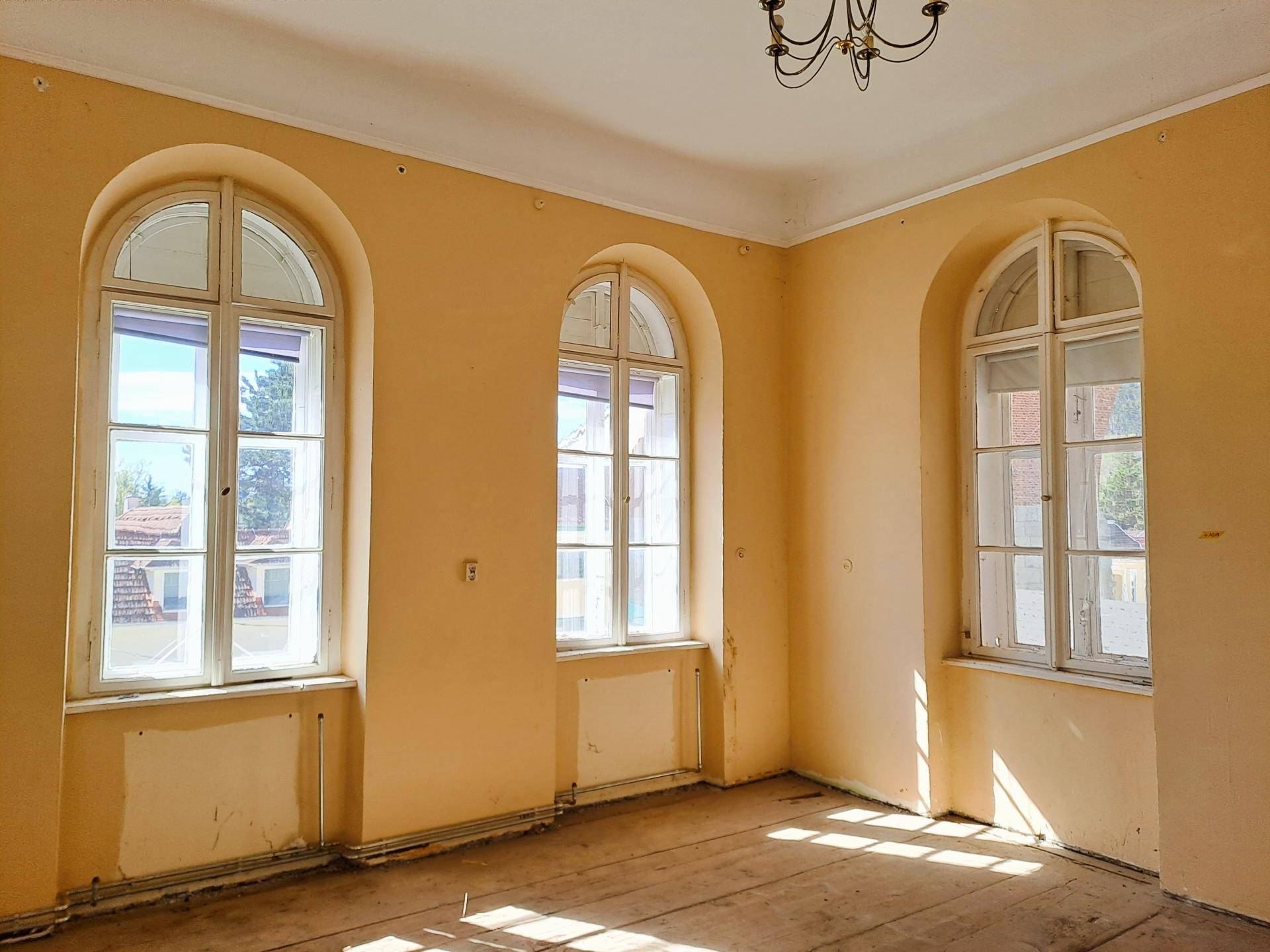 Geräumiger Raum mit gelben Wänden, hohen Decken und drei großen Rundbogenfenstern.