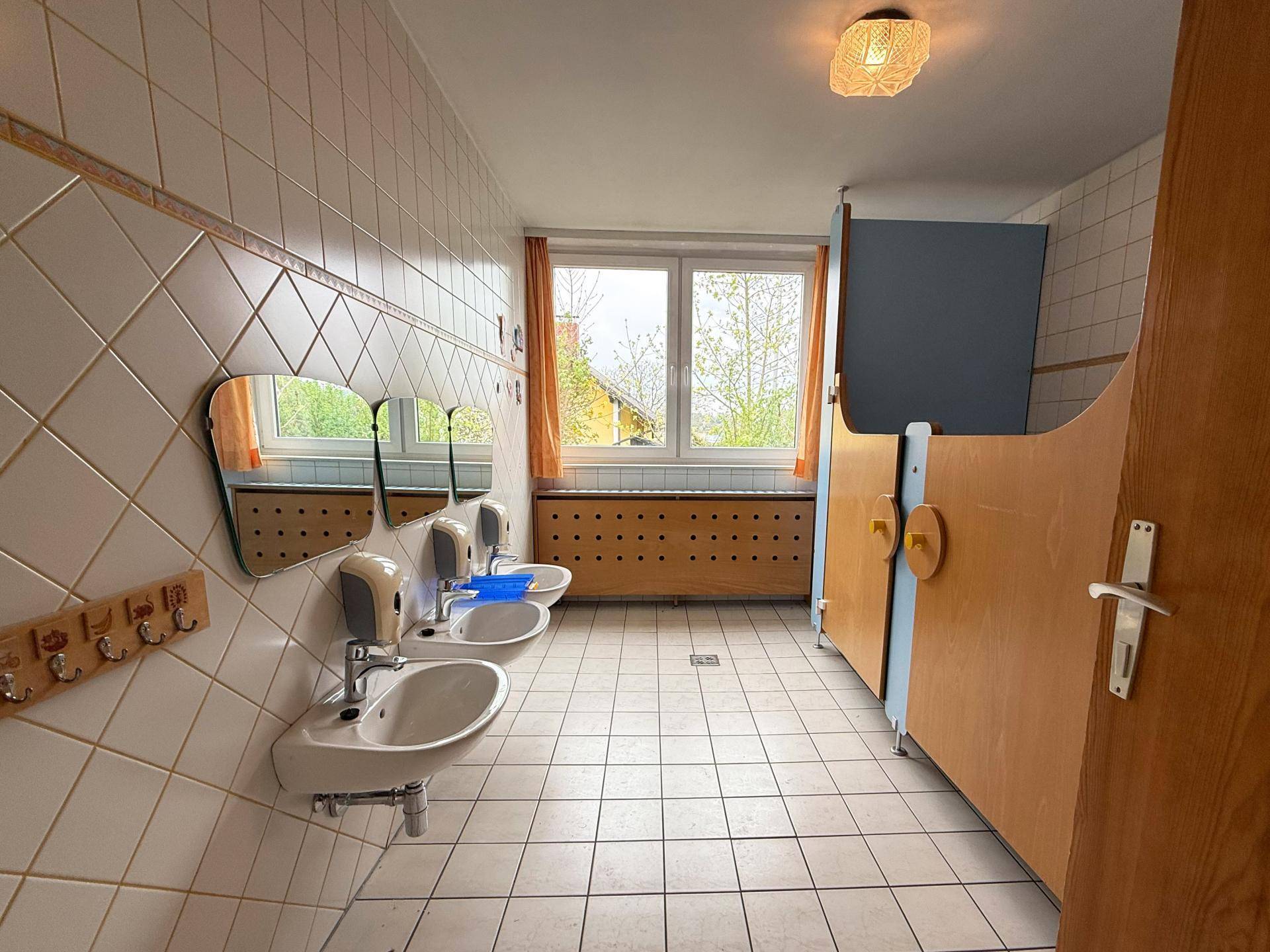 Waschraum mit mehreren Waschbecken, Fliesenboden und Fenster für natürliche Belüftung.