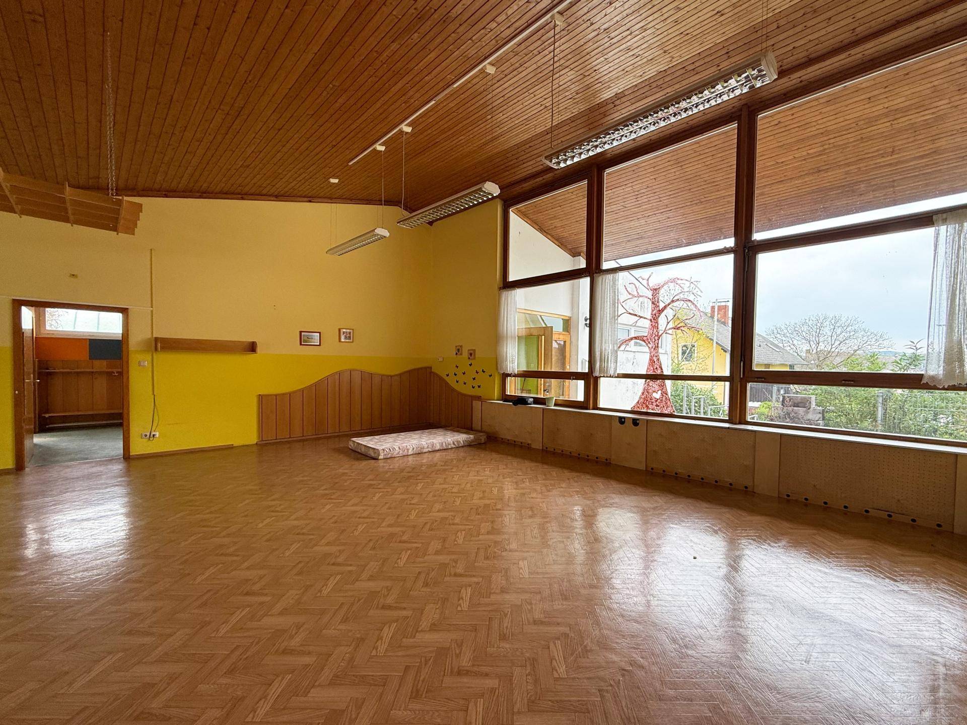 Geräumiger Wohnbereich mit Holzdecke, Parkettboden und großen Fenstern für viel Tageslicht und Blick ins Grüne.