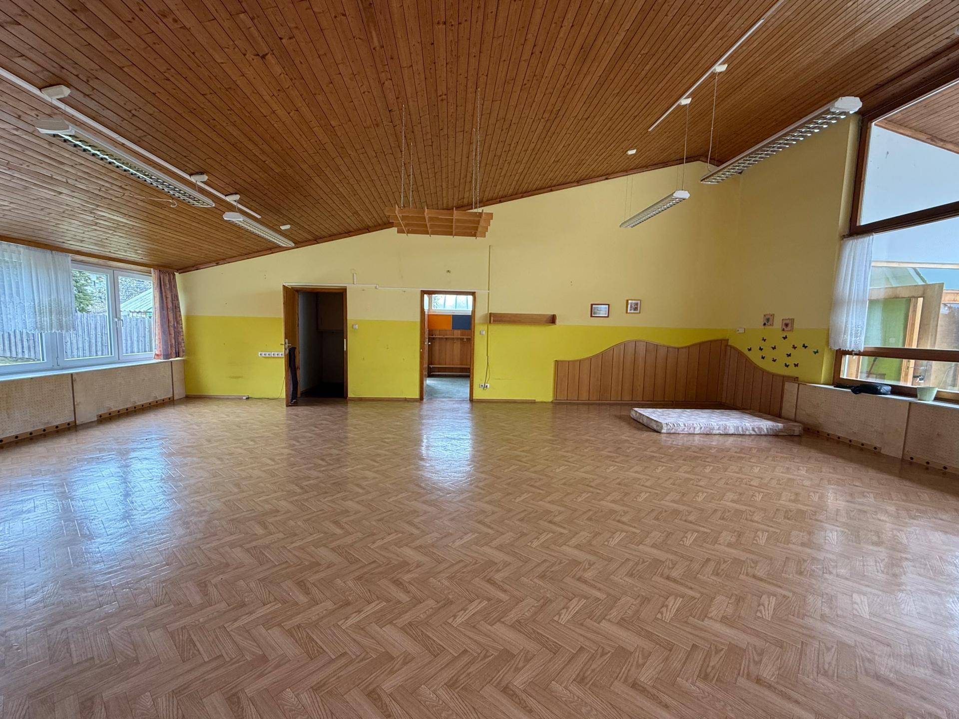 Großer, heller Raum mit Holzdecke und Parkettboden, ideal für vielfältige Nutzungsmöglichkeiten und mit Blick ins Grüne.