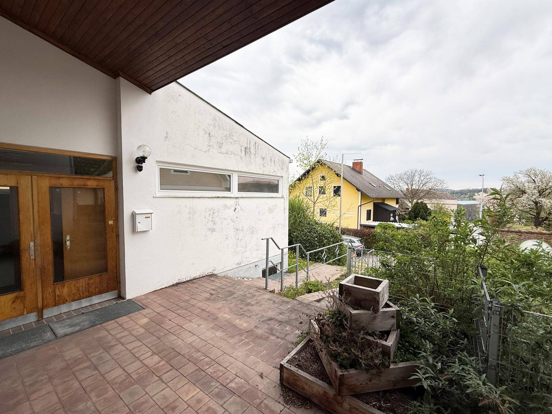 Eingangsbereich des Gebäudes mit gepflastertem Vorplatz und Blick auf die umliegende Landschaft.