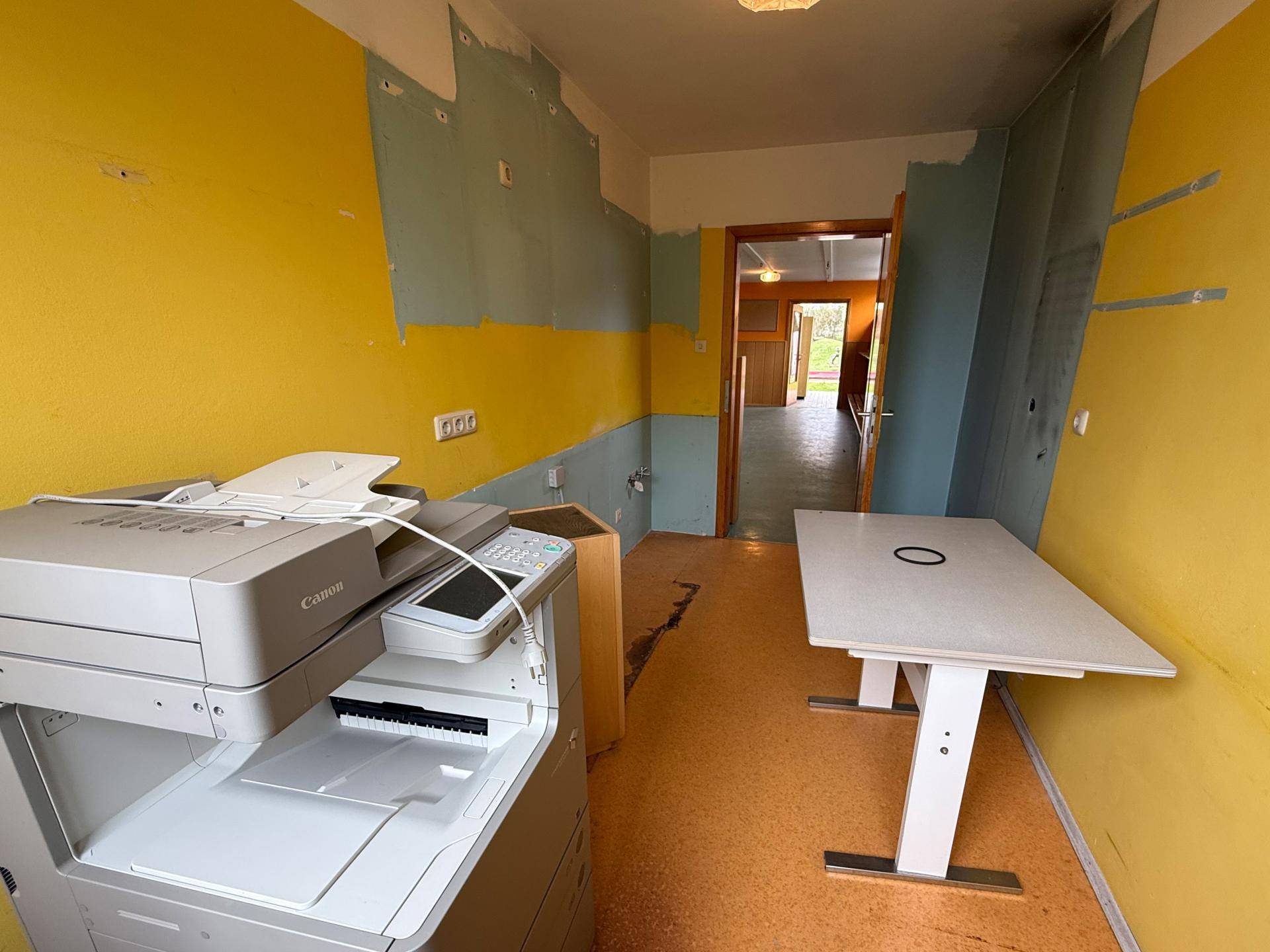Büroraum mit Drucker, Tisch und farbigen Wänden, bereit zur individuellen Gestaltung.