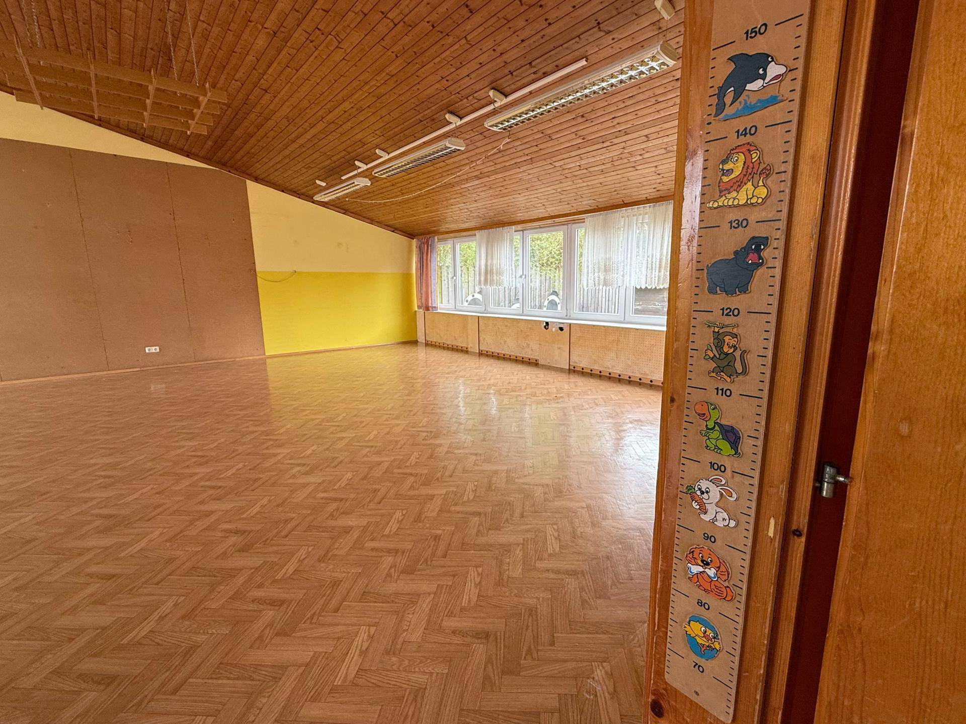 Großer, heller Raum mit Holzdecke und Parkettboden, ideal für Kinderaktivitäten und mit Blick ins Grüne.