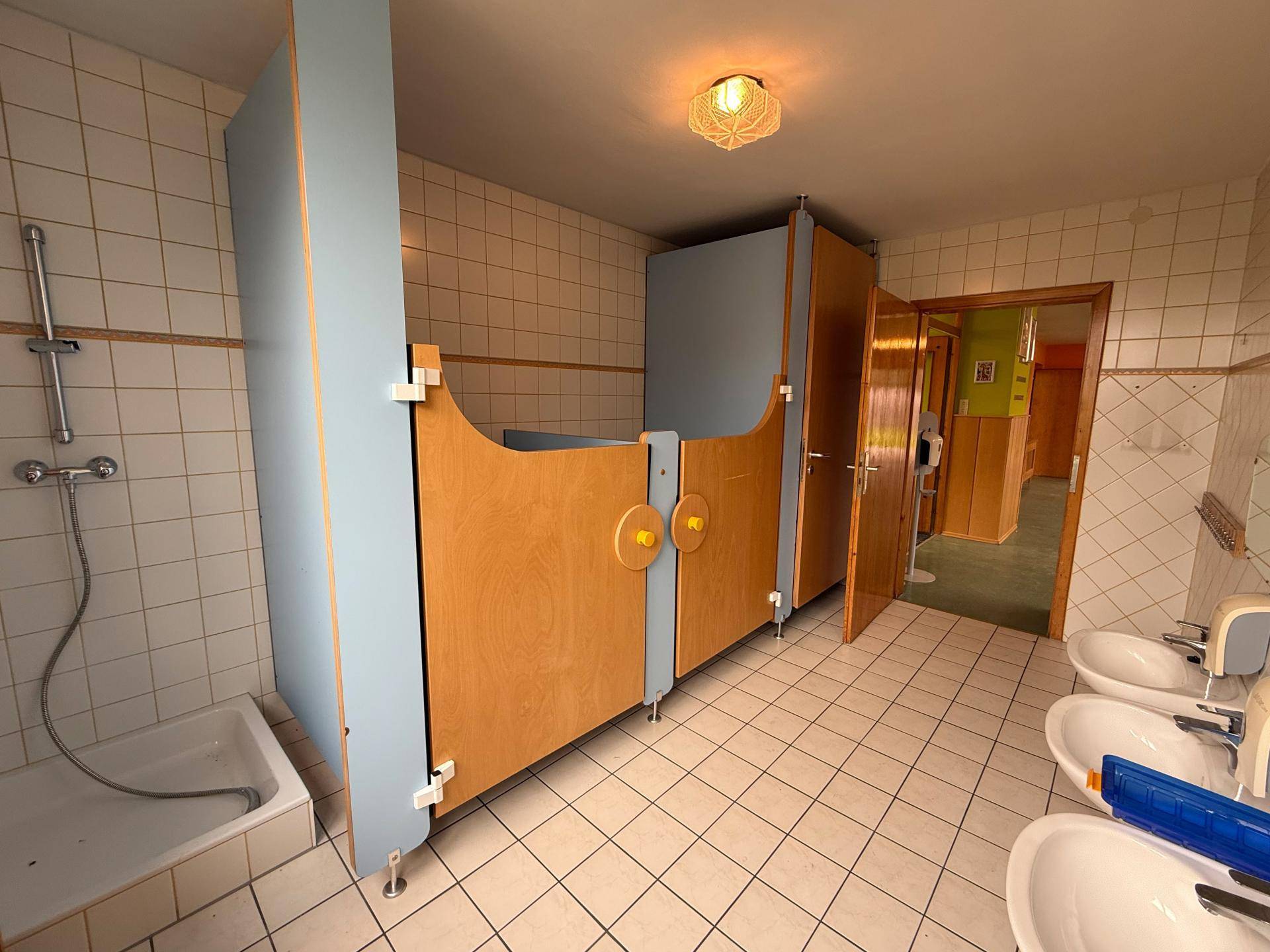 Sanitärbereich mit mehreren Waschbecken, Duschkabine und Fliesenboden.