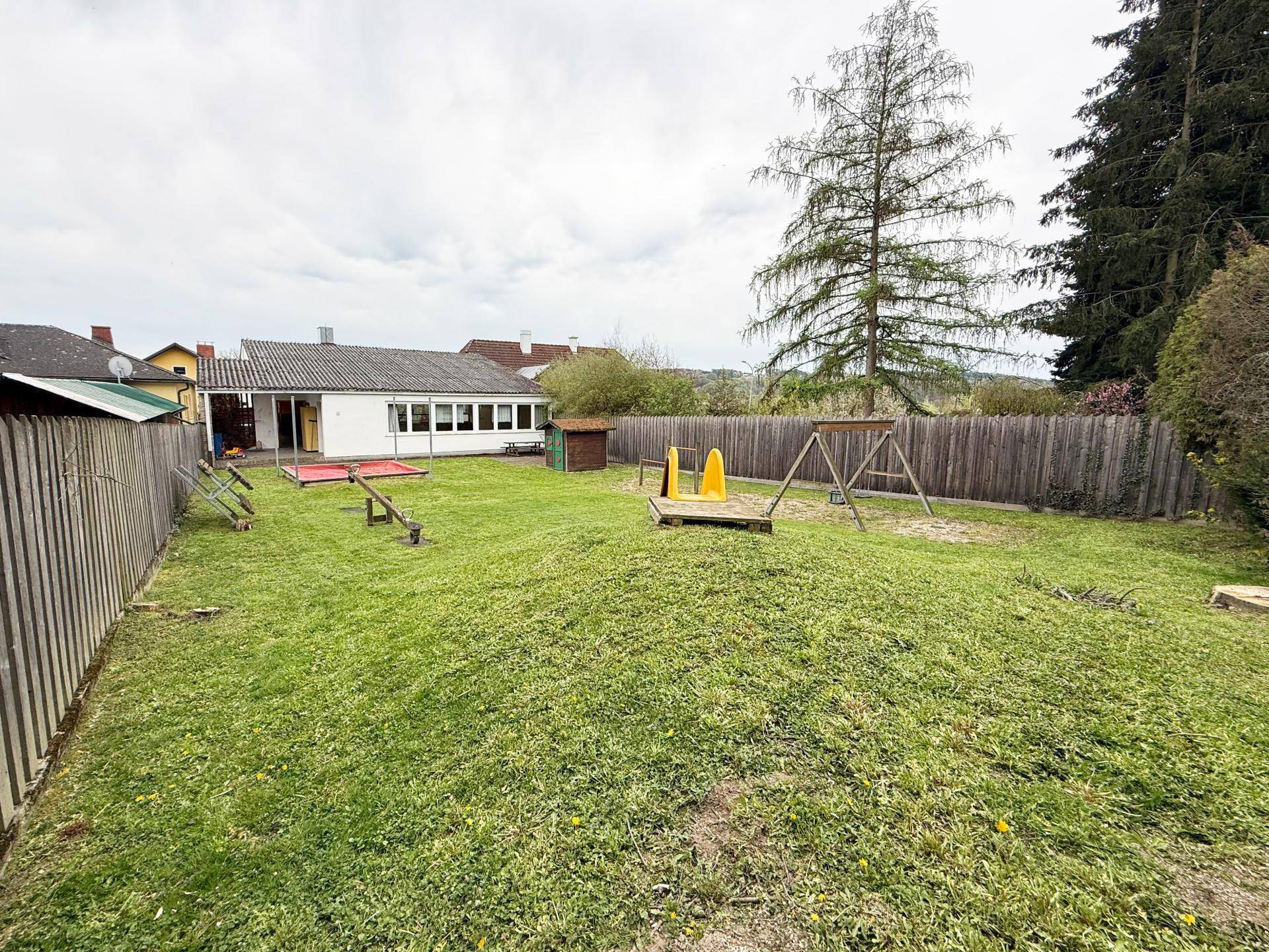 Großer Garten mit Rasen, Spielgeräten und viel Platz für Outdoor-Aktivitäten, umgeben von Bäumen.
