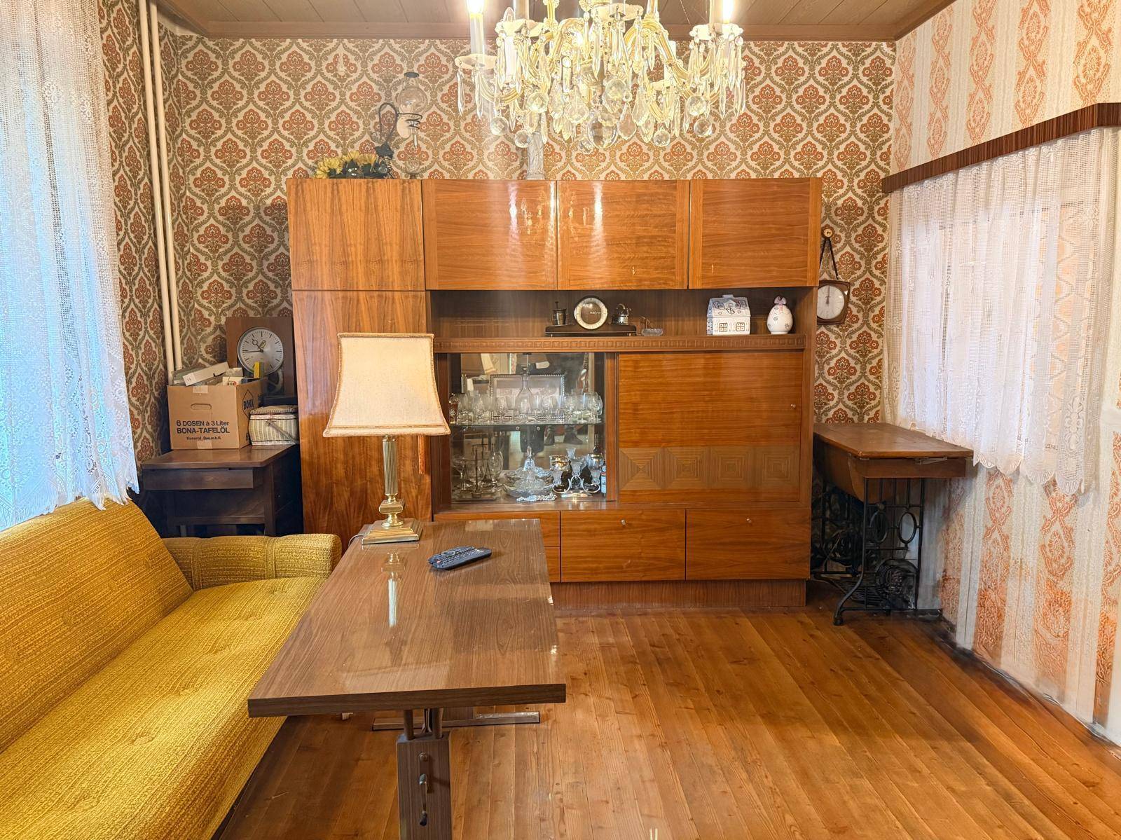 Wohnzimmer mit gelbem Sofa, Holzmöbeln und gemusterter Tapete im Vintage-Stil.