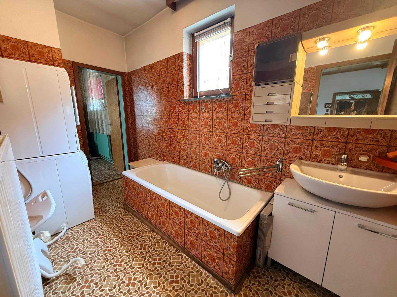Badezimmer mit Badewanne, Waschbecken und auffälligen orangefarbenen Fliesen im 80er-Jahre-Stil.
