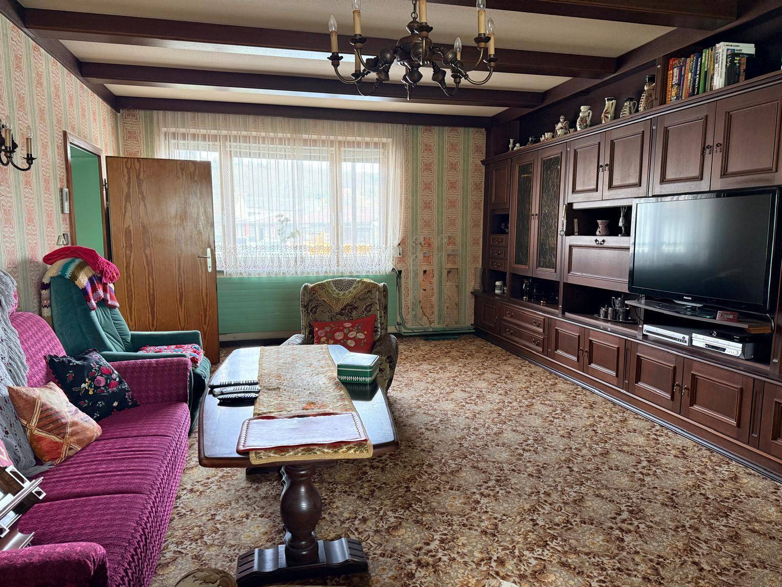 Wohnzimmer mit großem Holzschrank, Sofa und gemusterter Tapete im traditionellen Stil.