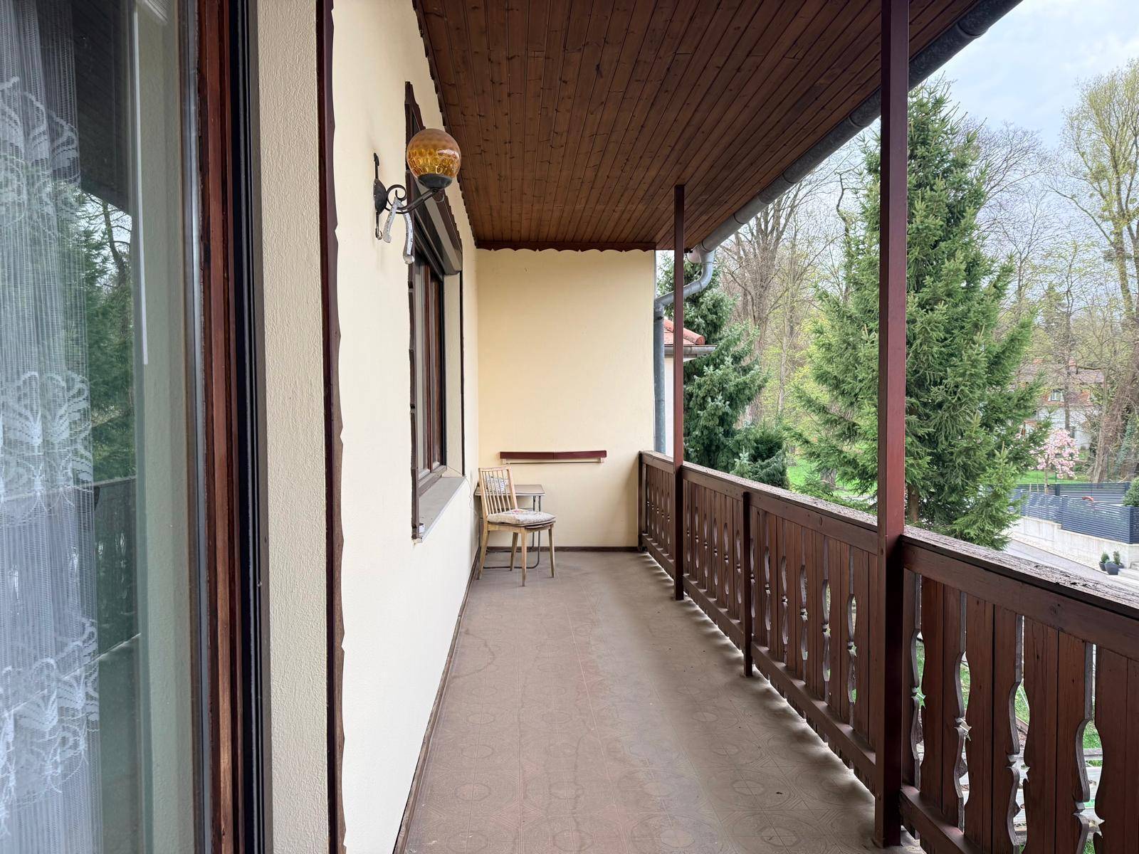Langer Balkon mit Holzgeländer und Blick ins Grüne, ausgestattet mit einem Stuhl.