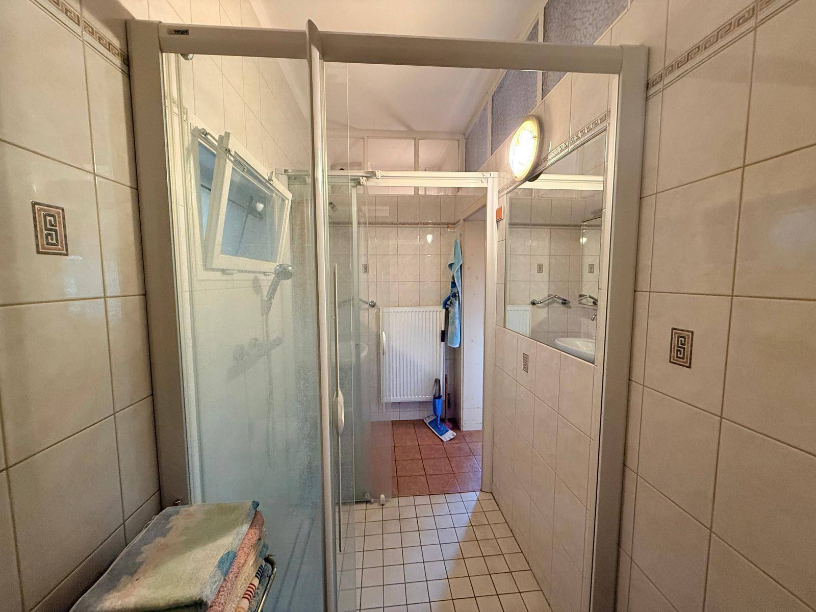 Badezimmer mit Duschkabine, hellen Fliesen und Fenster für Tageslicht.