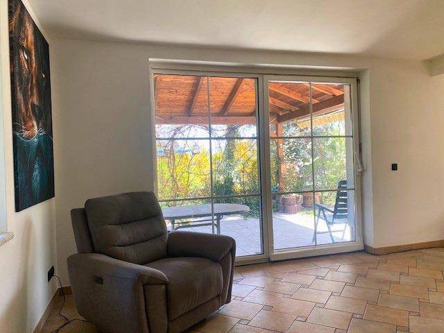 Gemütliches Wohnzimmer mit Sessel und großem Schiebefenster, das Zugang zur Terrasse bietet.