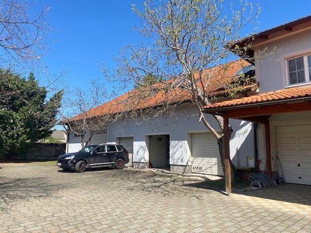 Seitenansicht des Gebäudes mit Garagen, Carport und gepflasterter Zufahrt an einem sonnigen Tag.