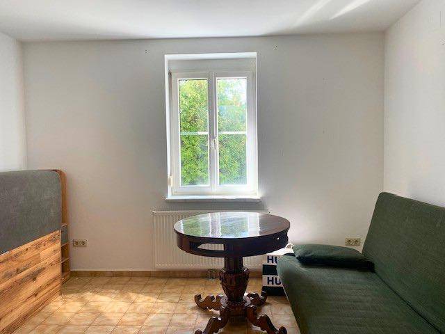 Helles Schlafzimmer mit Einzelbett, kleinem Tisch und Fenster mit Blick ins Grüne.