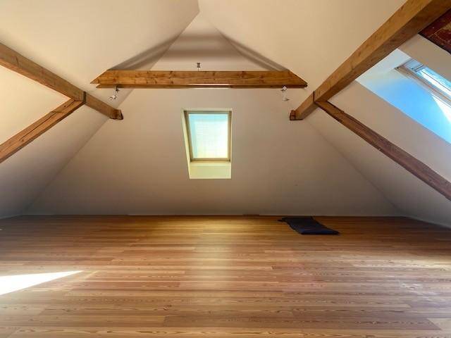 Heller Dachgeschossraum mit sichtbaren Holzbalken, Holzfußboden und Dachfenster.