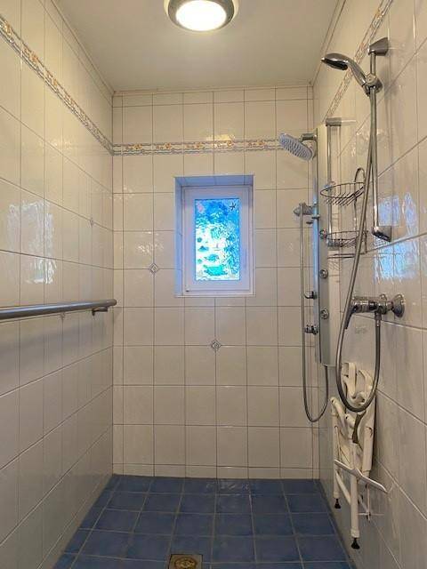 Barrierefreie Dusche mit Haltegriffen, Duschsitz und Fenster für natürliches Licht.
