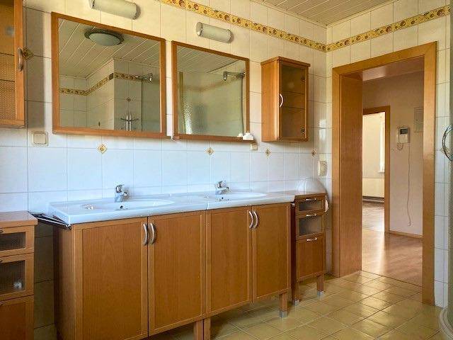 Badezimmer mit Doppelwaschbecken, Holzunterschränken und Fliesenboden in hellem Ambiente.