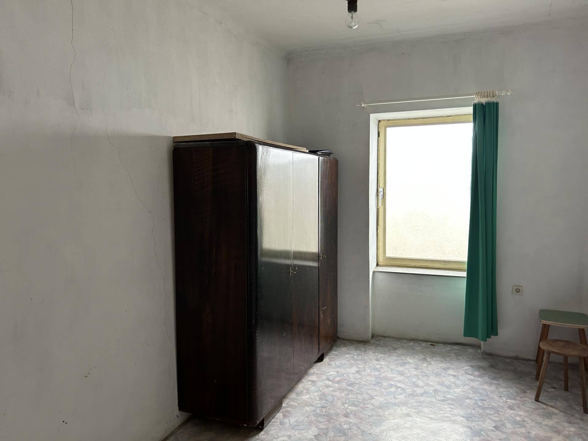 Einfaches Zimmer mit altem Kleiderschrank und einem Fenster, das Licht spendet.