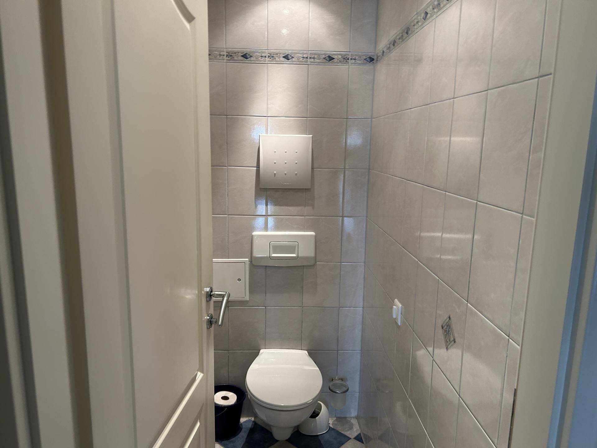 Gäste-WC mit hellen Fliesen und wandhängender Toilette in schlichtem Design.