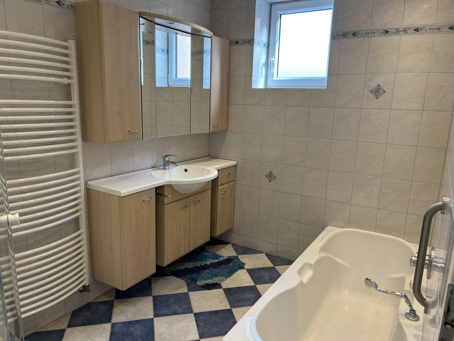 Badezimmer mit Badewanne, Waschtisch und einem Fenster, das für Belüftung sorgt.