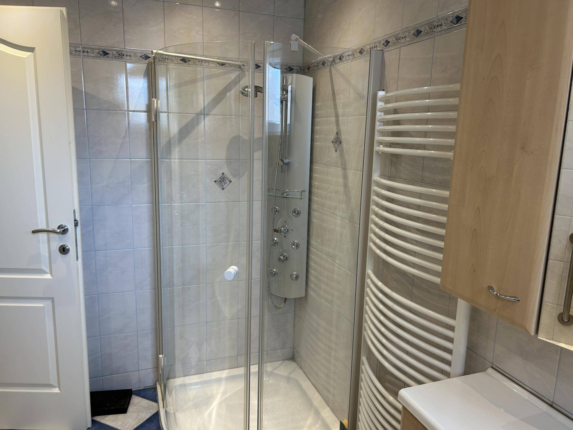 Modernes Badezimmer mit Duschkabine, Handtuchheizkörper und hellen Fliesen.