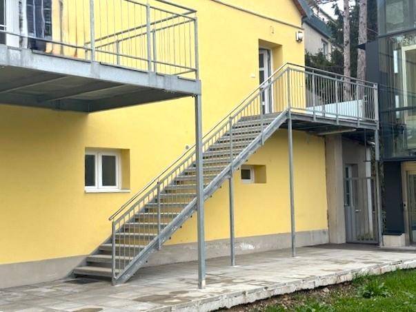 Gelbes Gebäude mit einer externen Metalltreppe, die zu einem oberen Balkon führt.