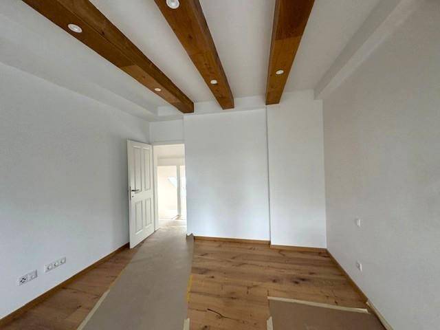 Helles Zimmer mit Holzbalken an der Decke und Holzboden, bereit für die individuelle Gestaltung.
