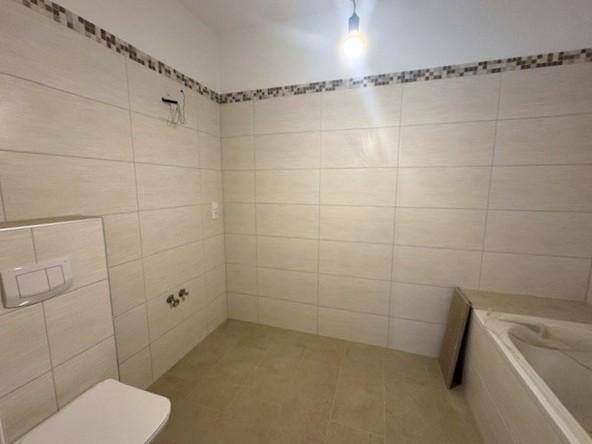 Badezimmer im Bau mit hellen Fliesen, wandhängendem WC und einer Badewanne.