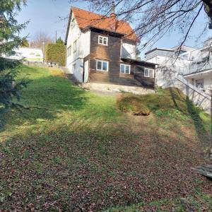 Haus auf einem Hanggrundstück mit rotem Ziegeldach, Holzverkleidung und großem Gartenbereich.