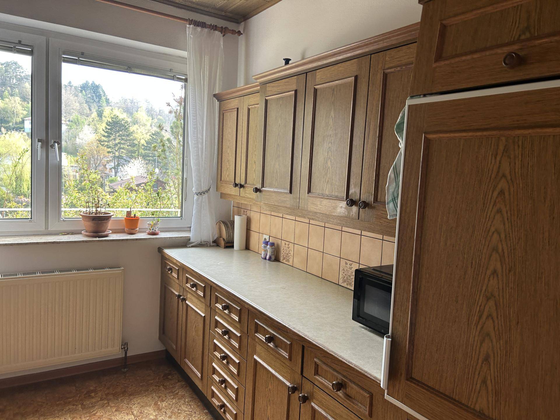 Rustikale Küche mit Holzschränken, Arbeitsplatte und Fenster mit Blick auf Bäume und Natur.