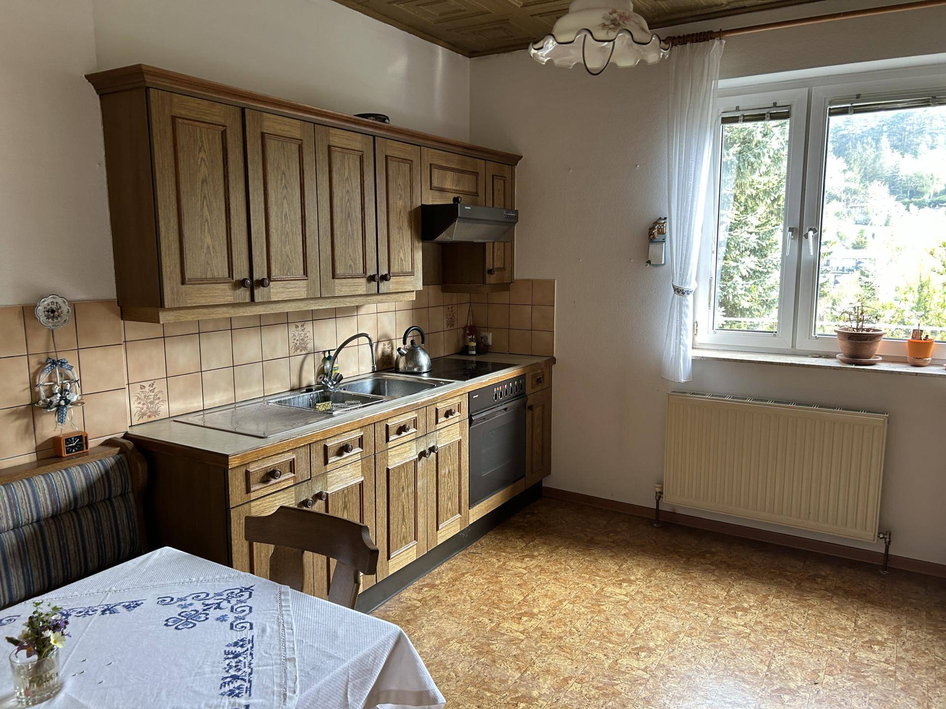 Traditionelle Küche mit Holzschränken, Spüle und Blick ins Grüne durch das Fenster.
