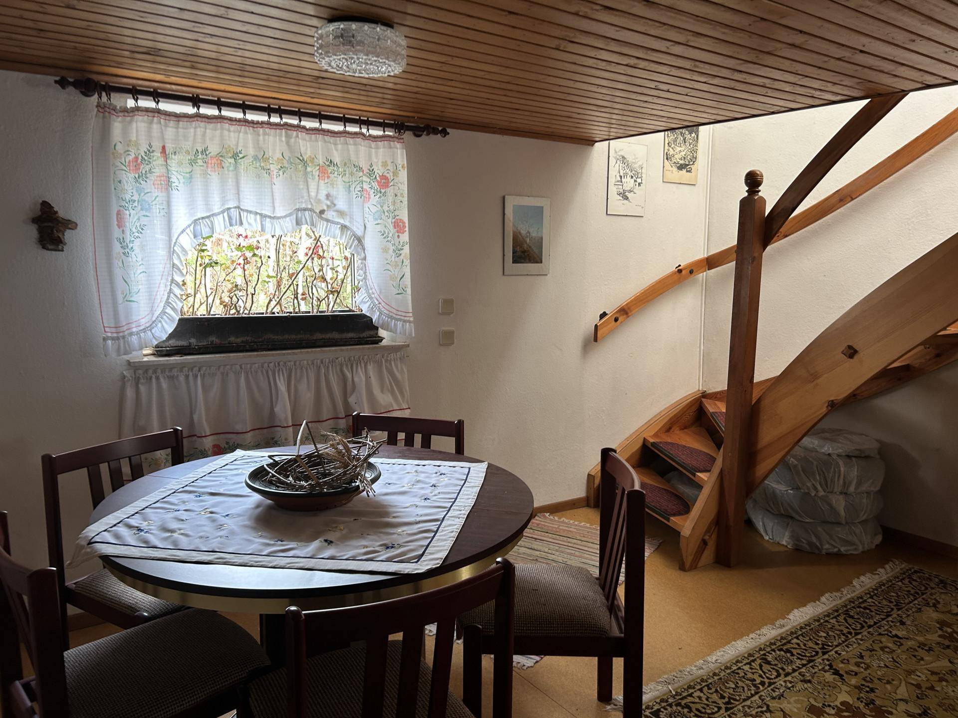 Essbereich mit Holztisch, Stühlen und Treppe, Fenster mit Blick ins Grüne.