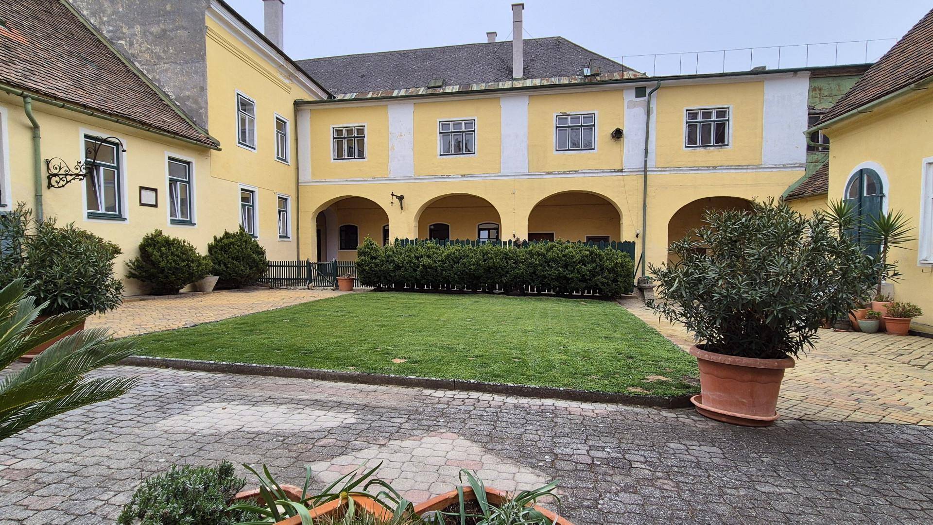 Großer Innenhof mit Rasenfläche, gepflastertem Bereich und Arkadengang.