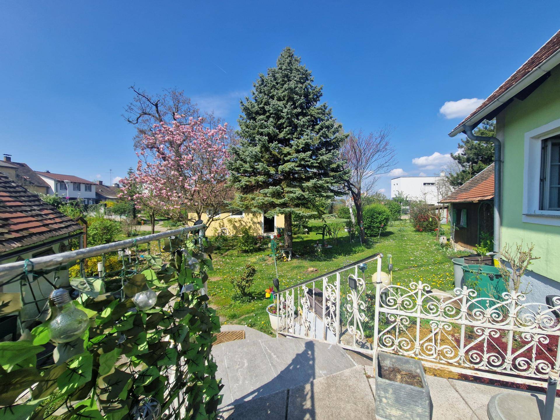 Terrasse mit schmiedeeisernem Geländer und Blick auf den weitläufigen Garten mit Bäumen.