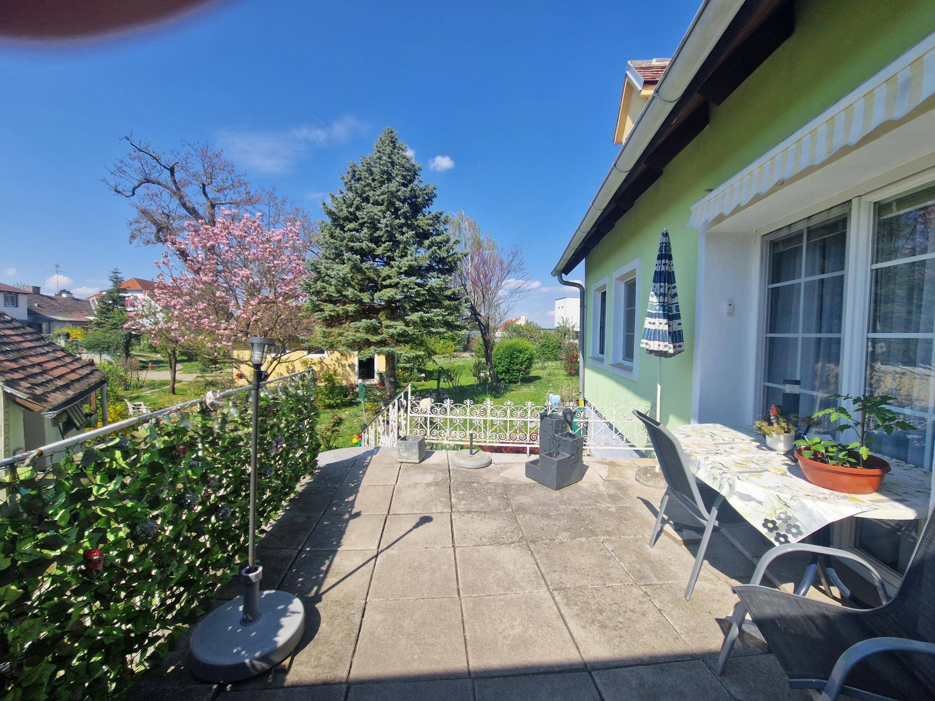 Geräumige Terrasse mit Fliesenboden, Gartenmöbeln und Blick ins Grüne an einem sonnigen Tag.