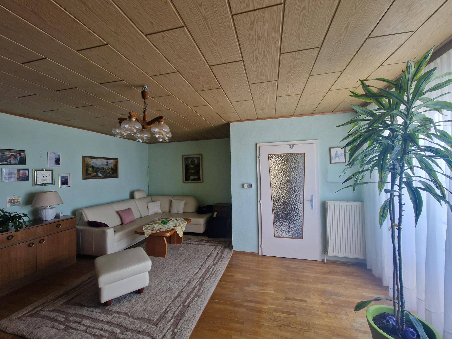 Gemütliches Wohnzimmer mit heller Couch, Holzdecke und Parkettboden in traditionellem Stil.