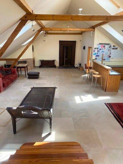 Geräumiges Dachgeschoss mit Fliesenboden, sichtbaren Holzbalken und viel Tageslicht durch Dachfenster.