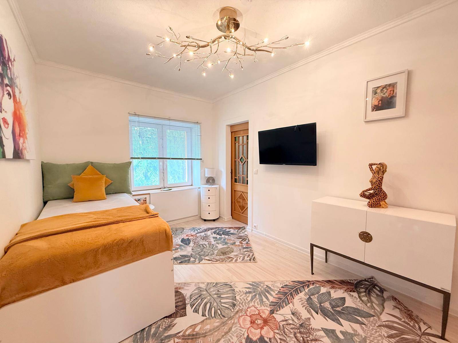Helles Schlafzimmer mit Einzelbett, modernen Möbeln und floralen Teppichen.