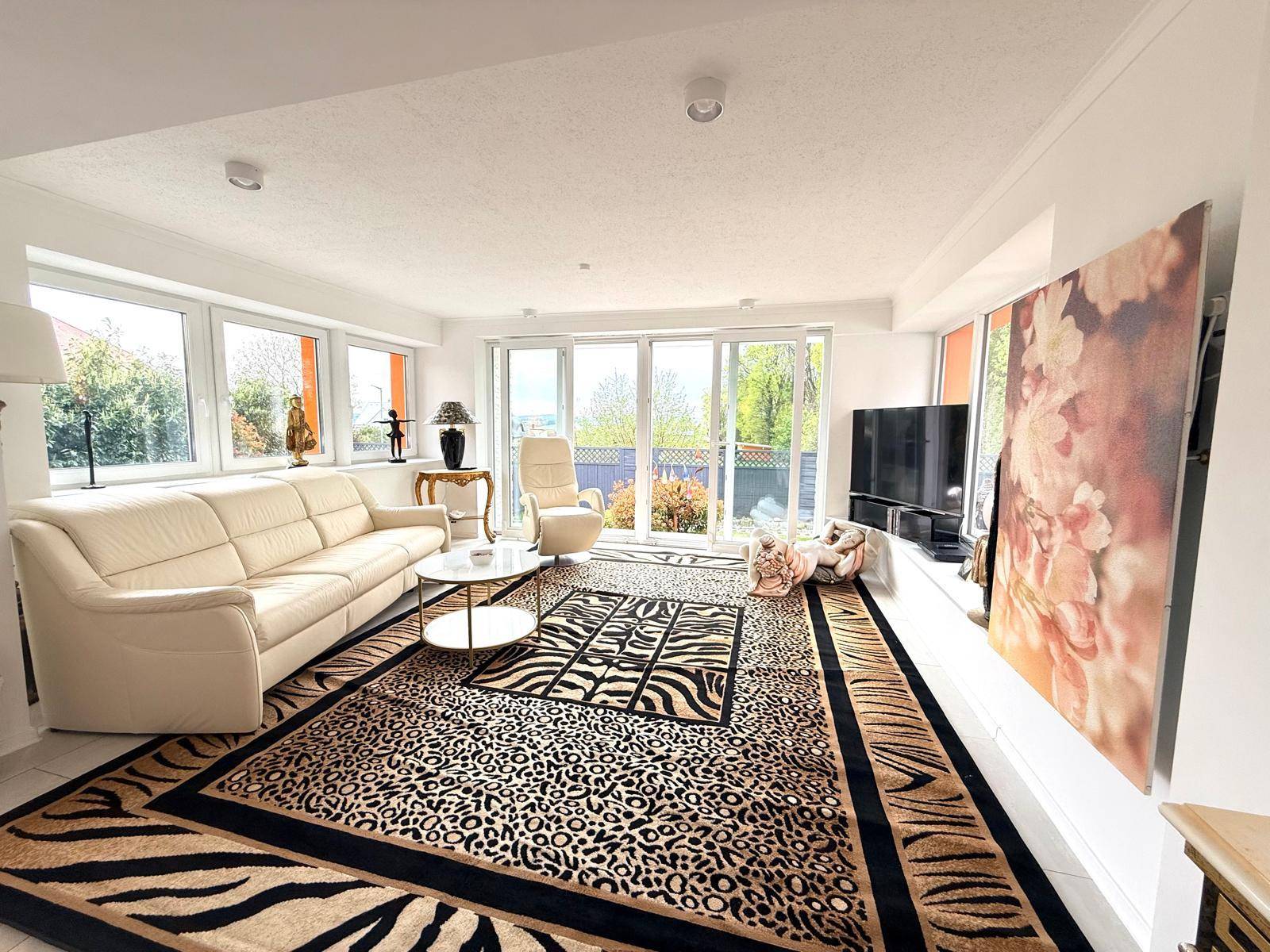 Helles Wohnzimmer mit großen Fenstern, beigem Sofa und Blick ins Grüne.