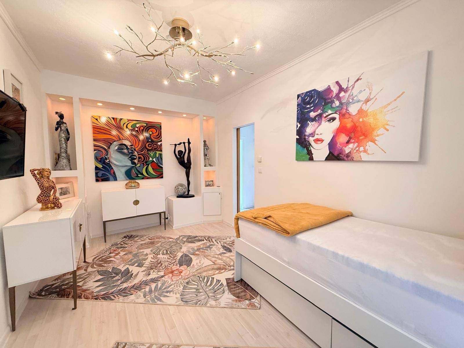 Modern eingerichtetes Schlafzimmer mit Kunstwerken, Einzelbett und heller Atmosphäre.