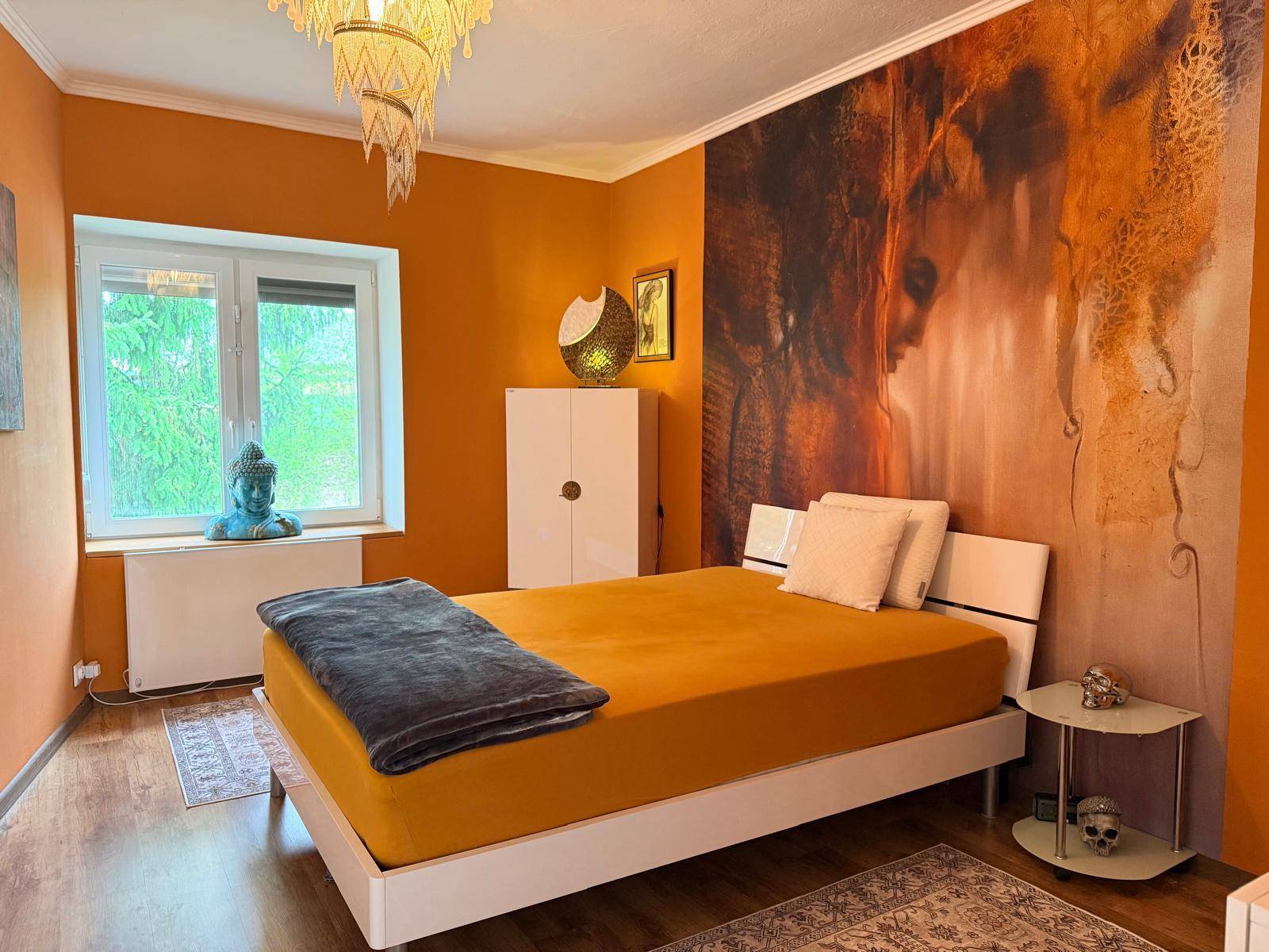 Schlafzimmer mit orangefarbenen Wänden, großem Bett und dekorativer Wandtapete.