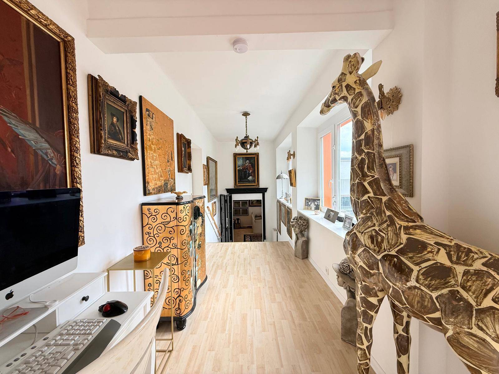 Langer Flur mit Holzboden, Kunstwerken und dekorativer Giraffenstatue.